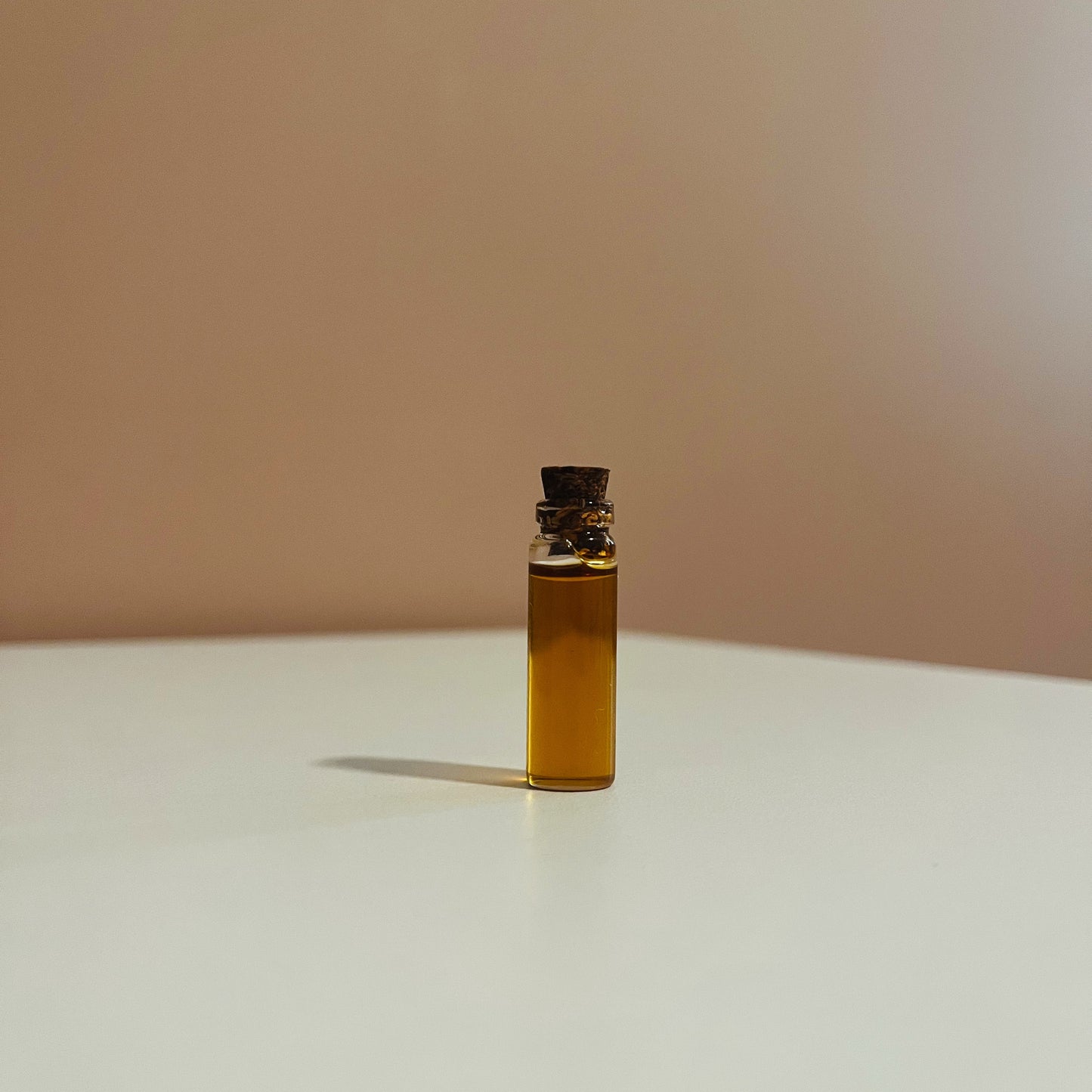 Small glass bottle with cork stopper containing demulcere facial oil Serum on a white surface with a beige background