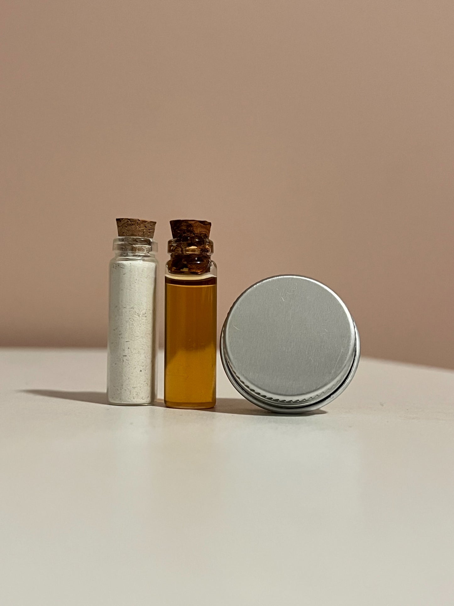 2g glass vial filled with powdered cleanser beside 2g glass vial filled with facial oil serum beside 5g silver tin filled with balm
