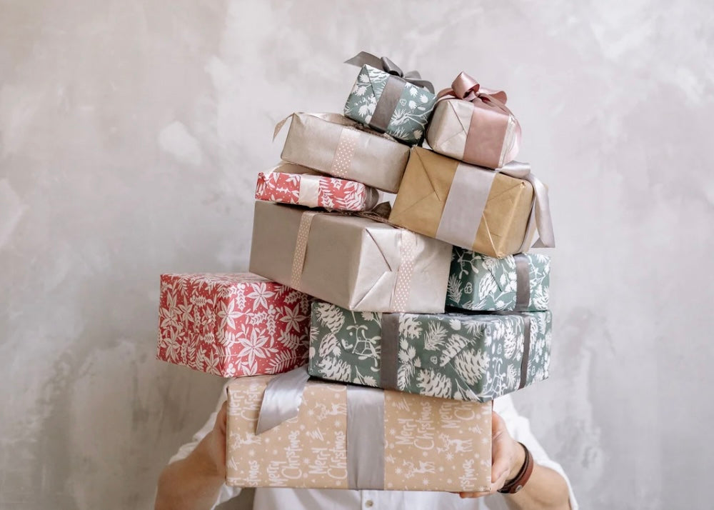 person holding stack of wrapped gifts against neutral background