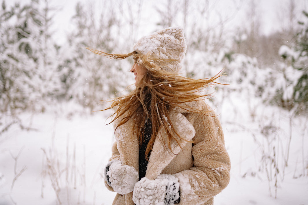 woman in winter clothing spinning in the snow with trees in the backgroun