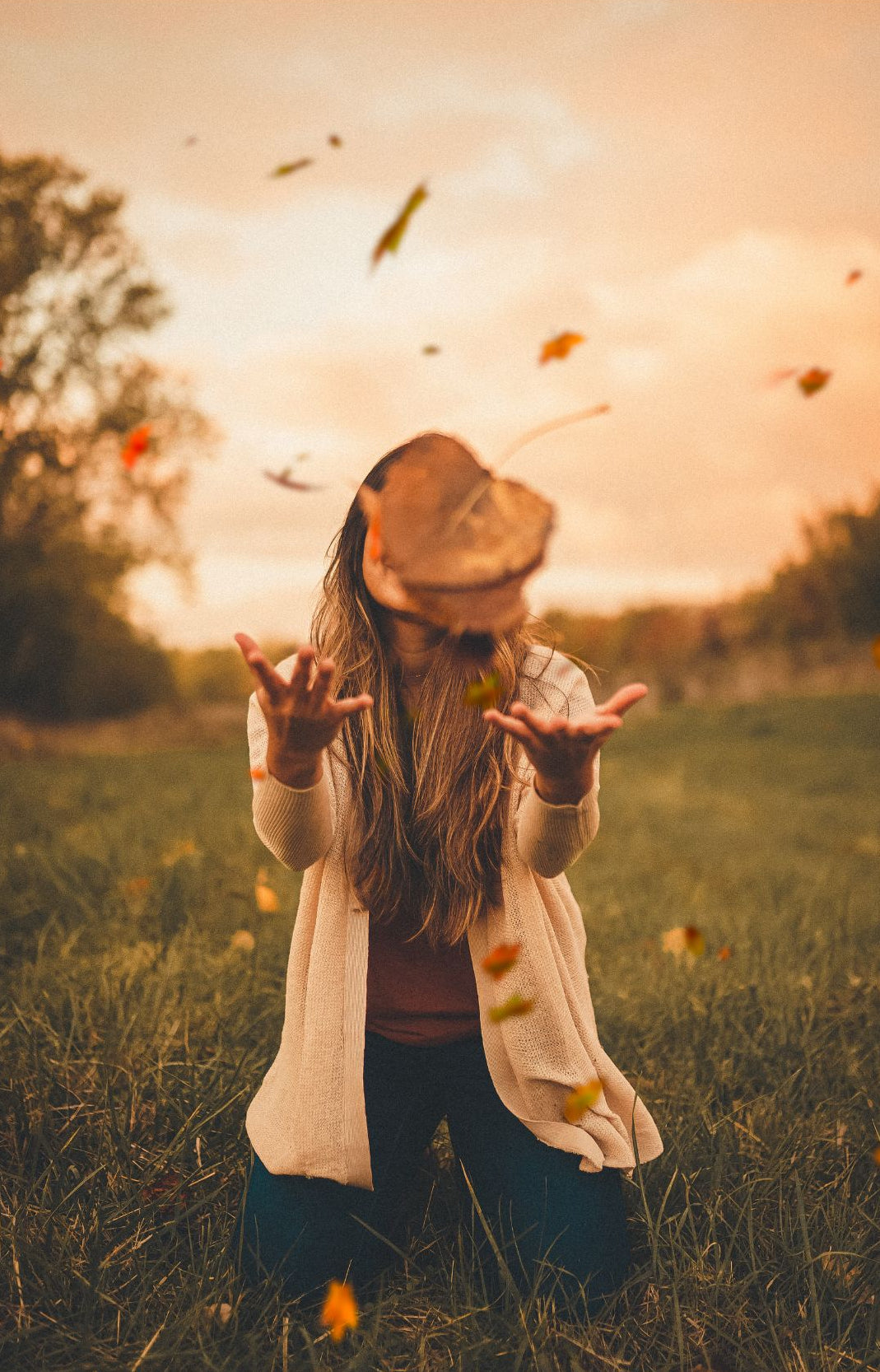 woman kneeling on grass throwing autumn leaves