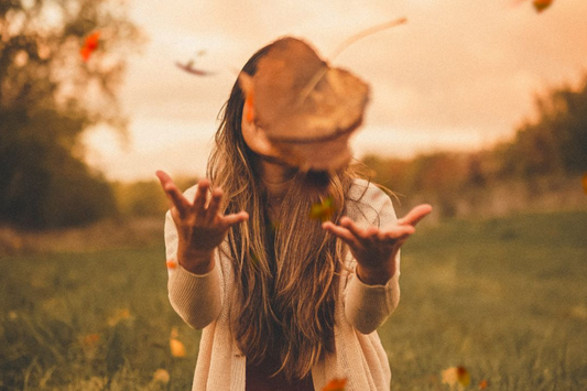 Woman smiling and tossing autumn leaves in a field