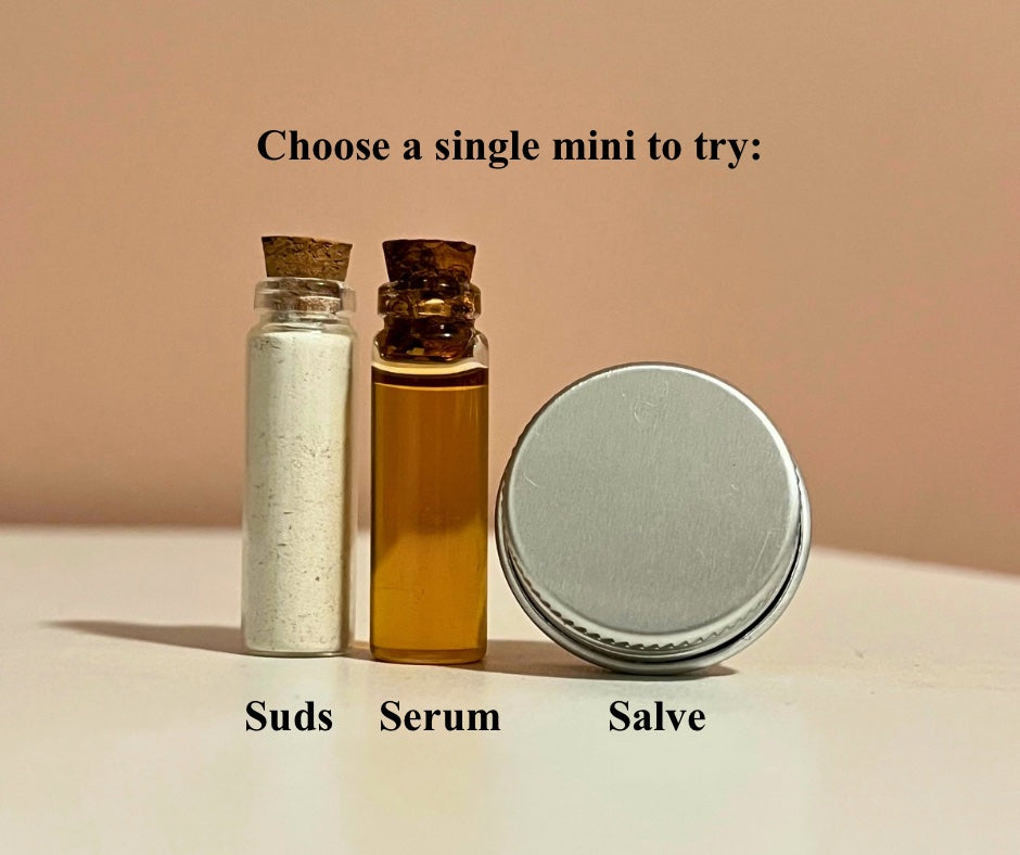 Three small glass containers labeled 'Suds', 'Serum', and 'Salve' with a beige background.