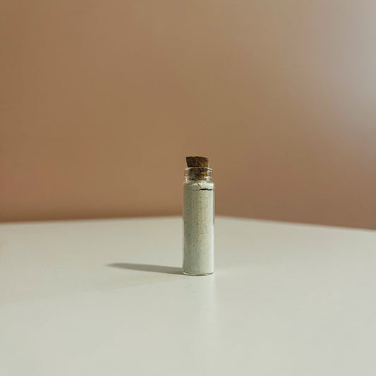 Small glass bottle filled with demulcere Suds powdered facial cleanser with cork lid on a beige surface and background